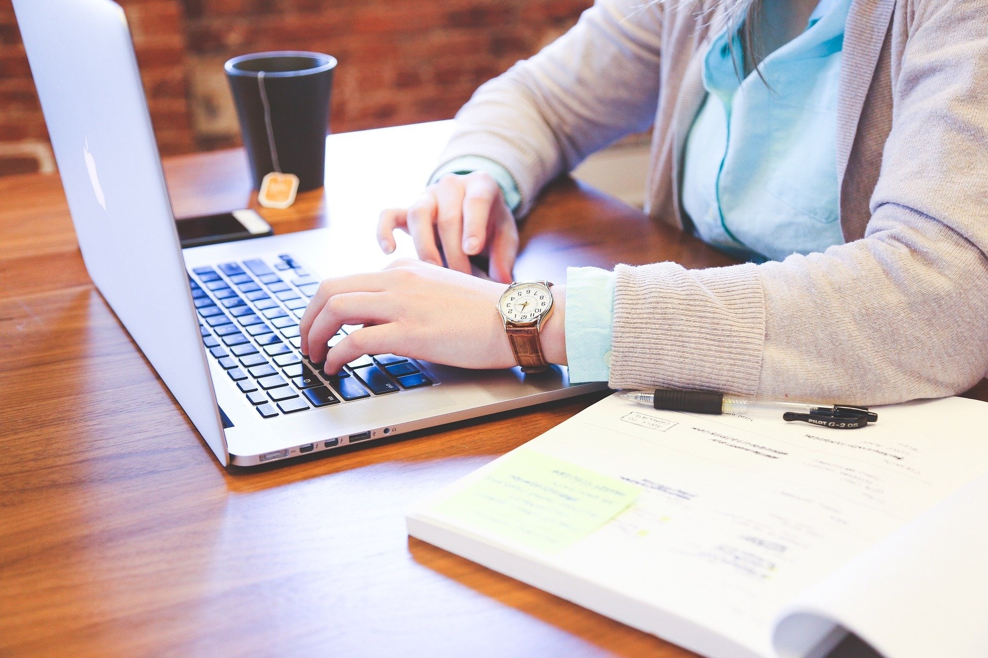 Woman typing on a laptop with a book open