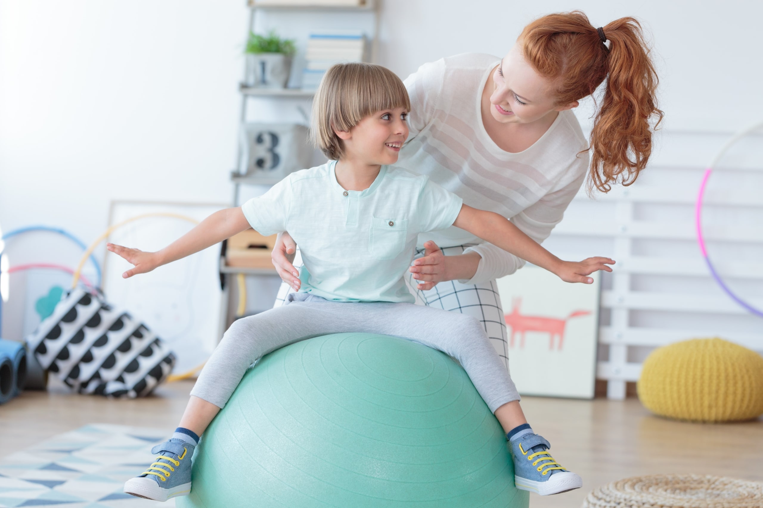Physical Therapist Assistant helping a young boy sit on a ball