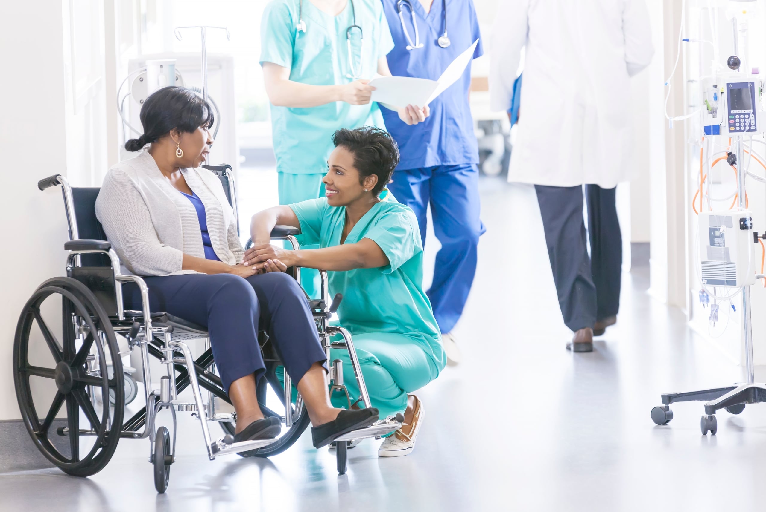 African-American nurse kneeling beside a patient in a wheelchair