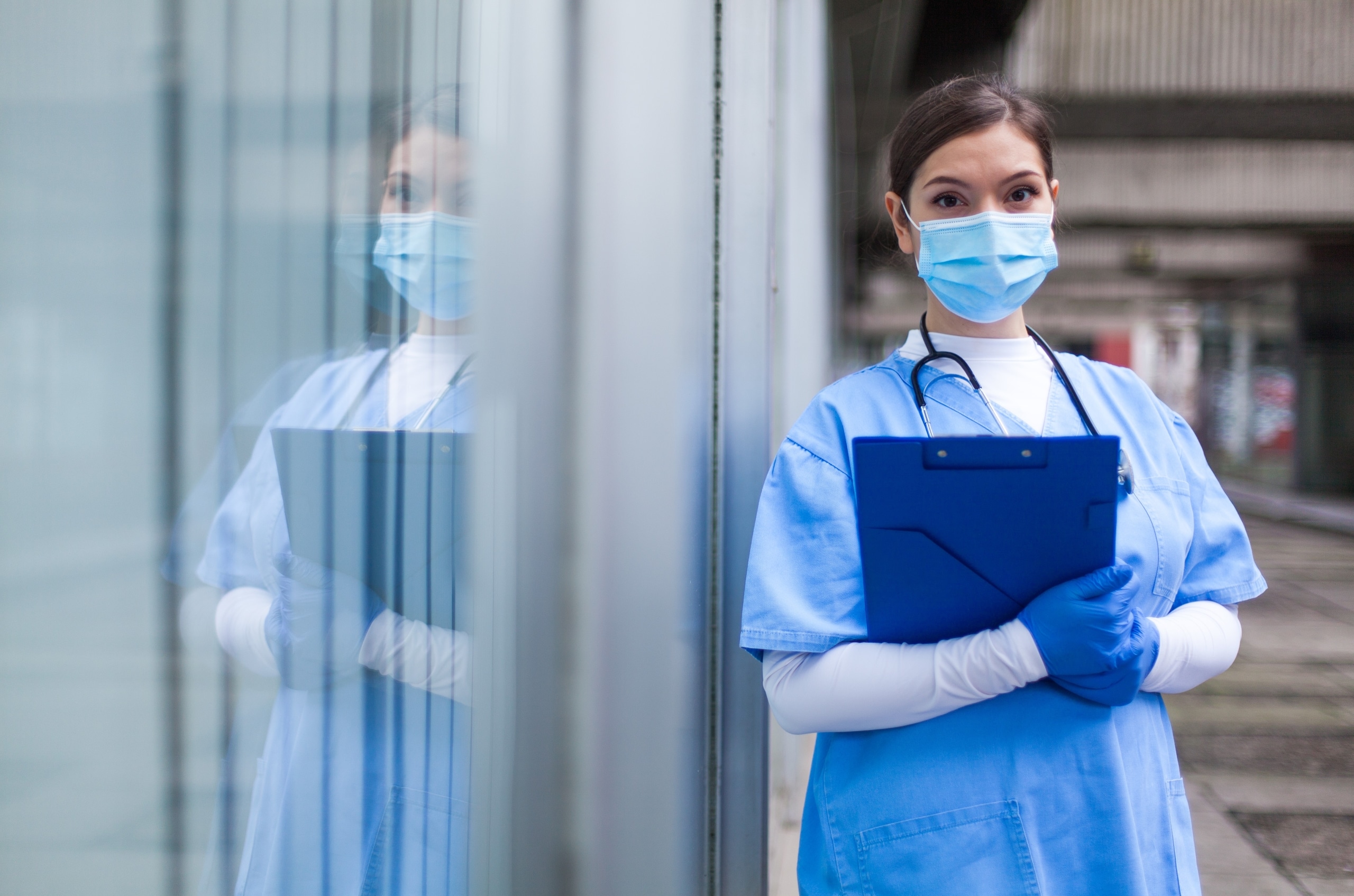 Masked nurse with a clipboard standing outside