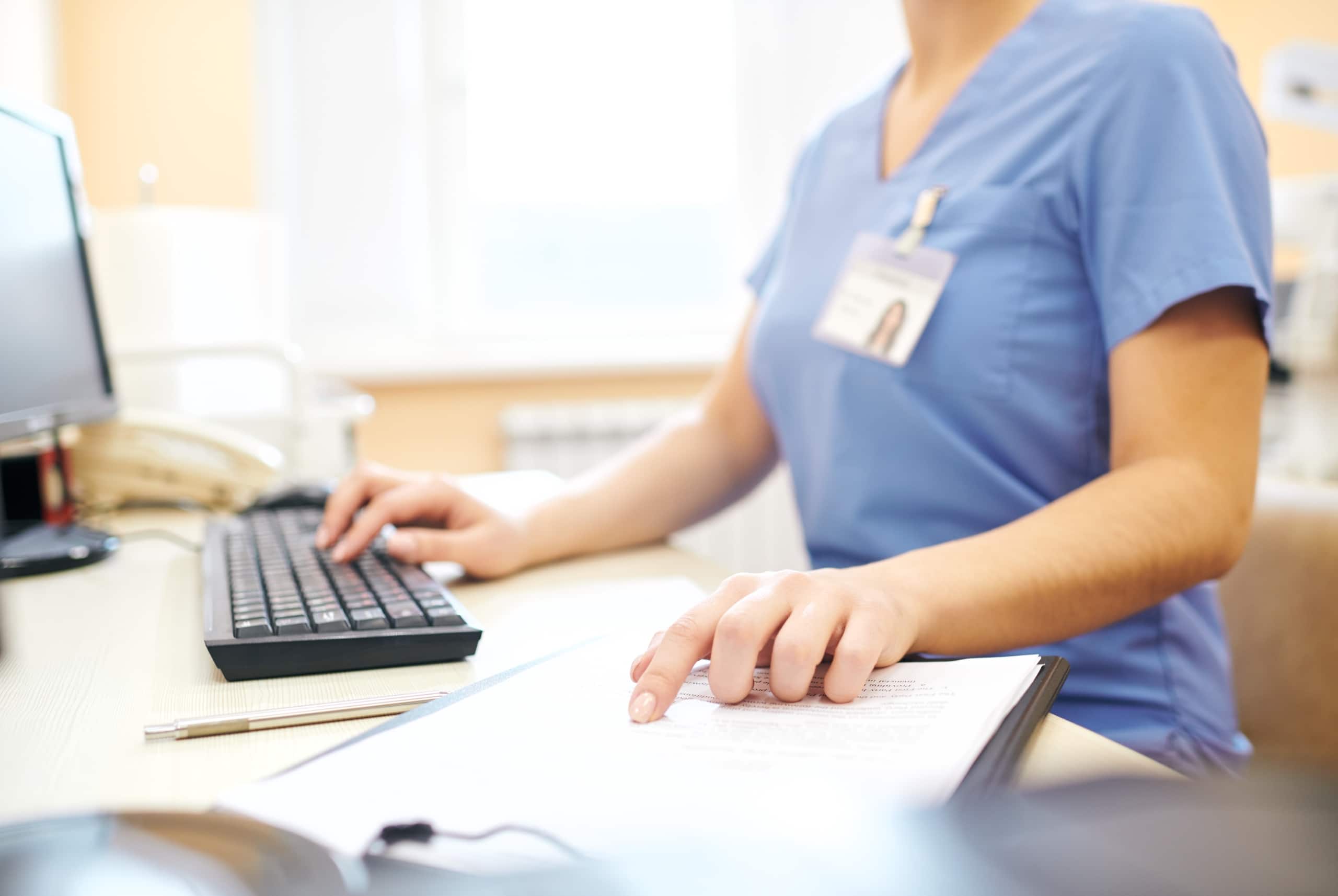 Close up of a nurse in scrubs using a computer