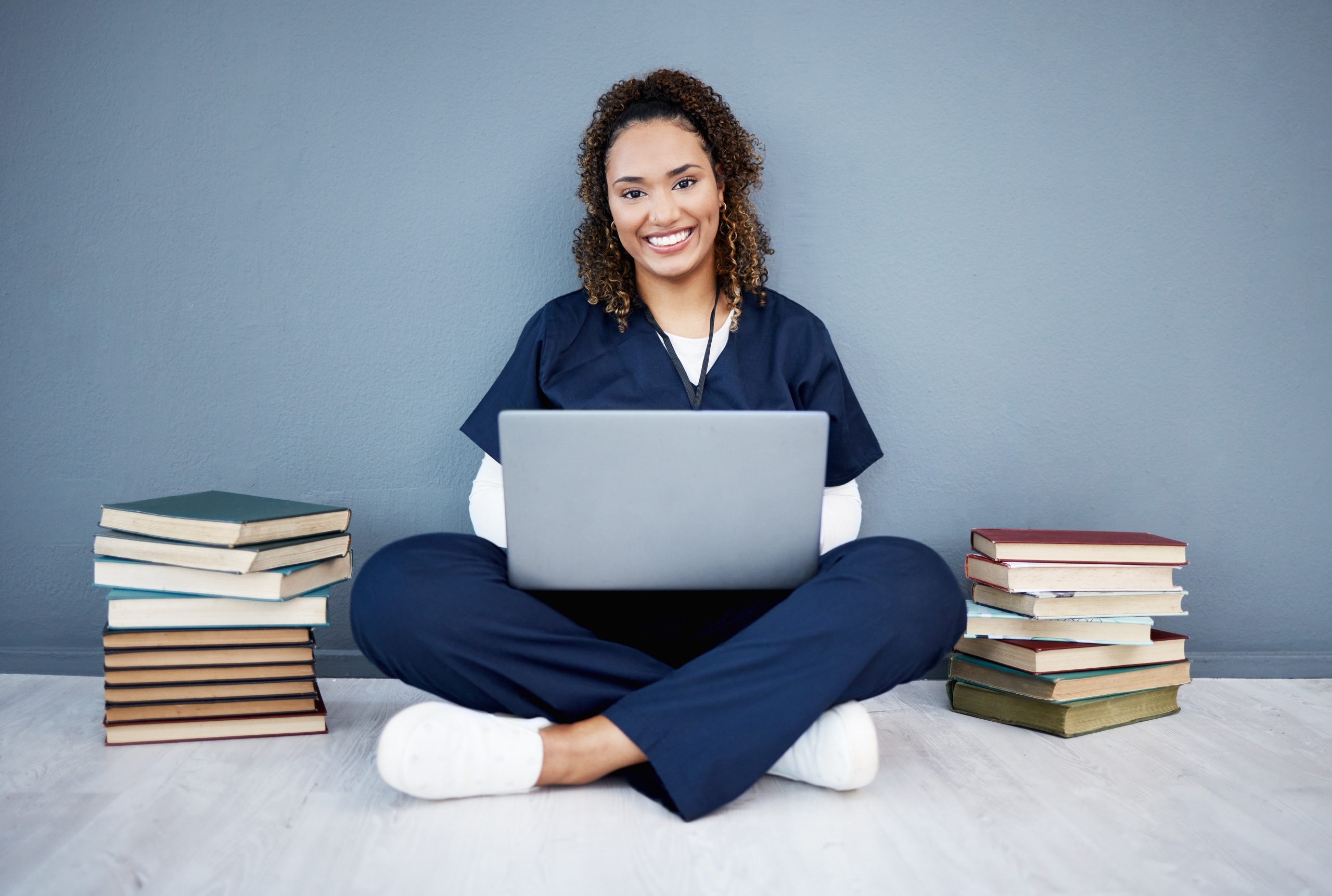 African-American nurse sitting on the ground with a laptop and stacks of books