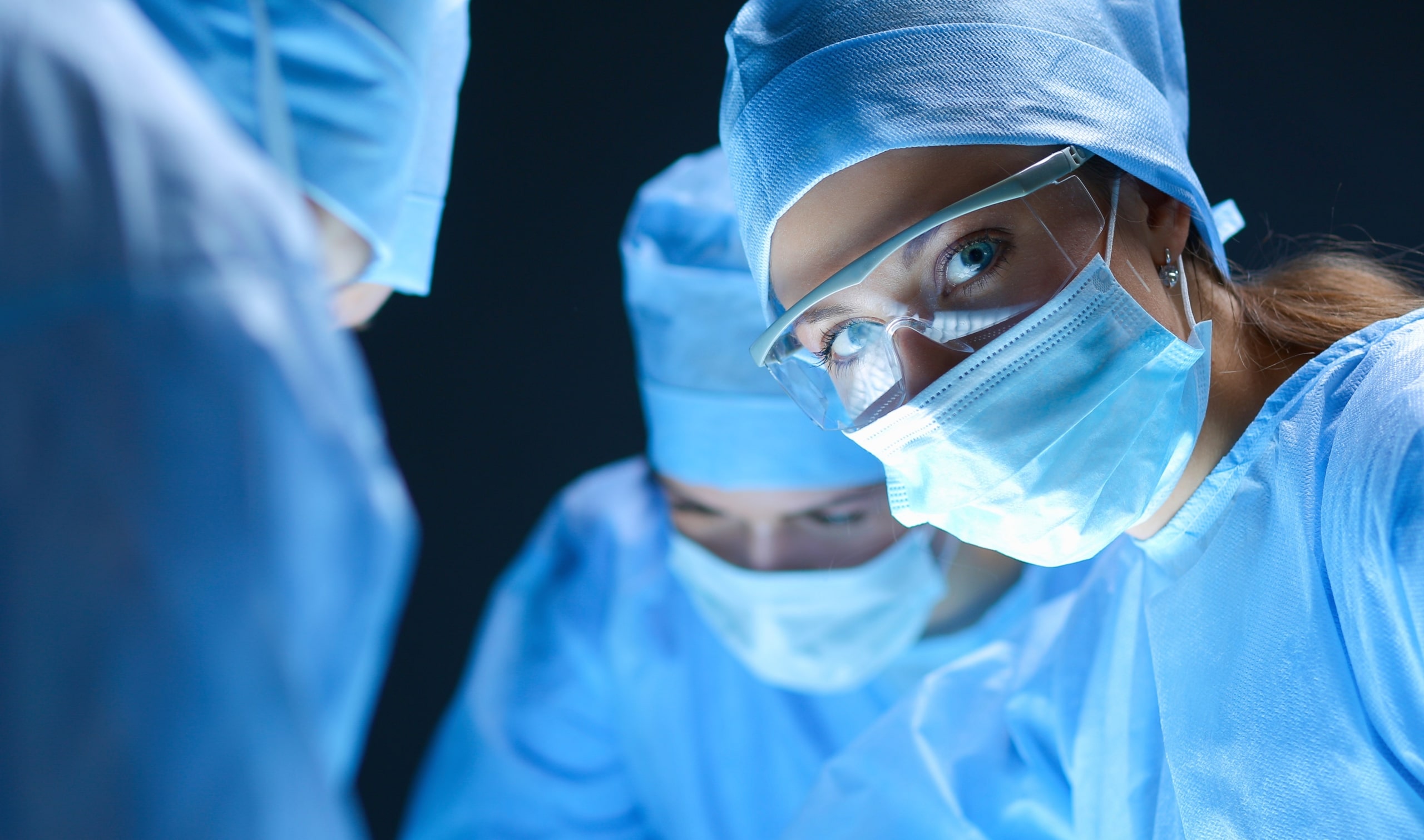 Masked woman standing beside a surgical team