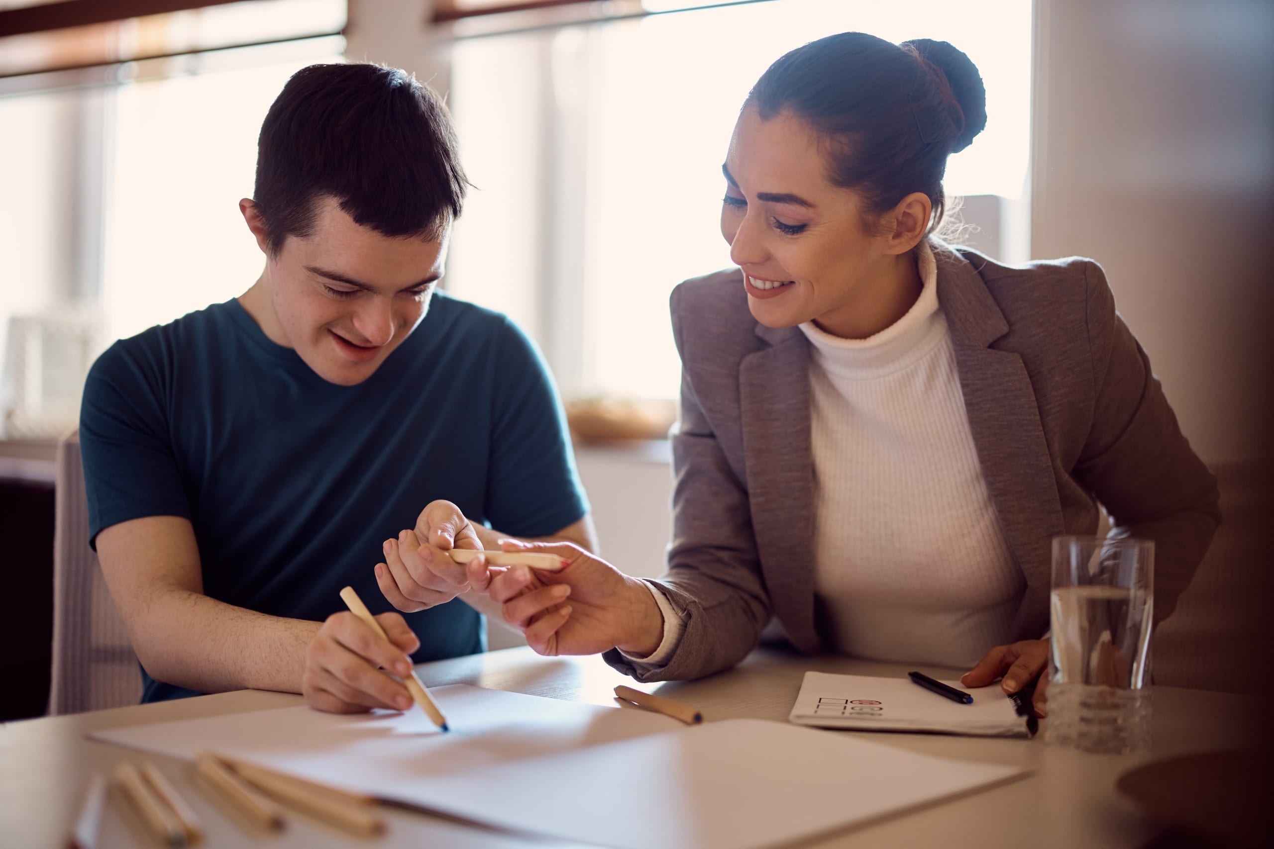 Woman helping a young man with down syndrome at a table