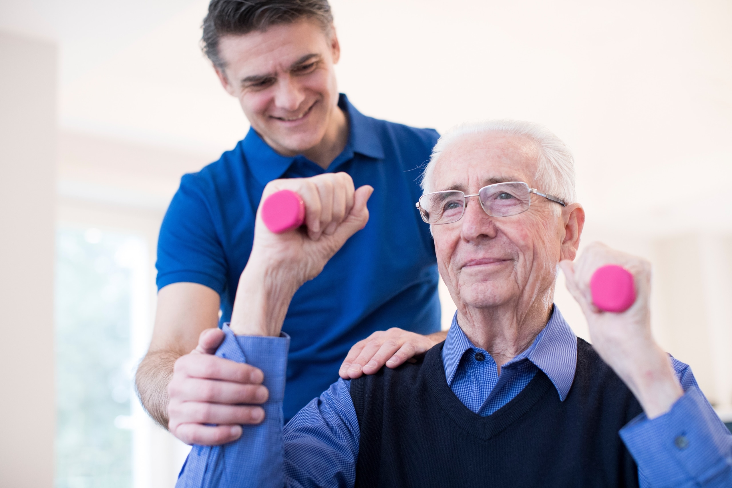 Physical therapy professional helping an elderly man lift weights