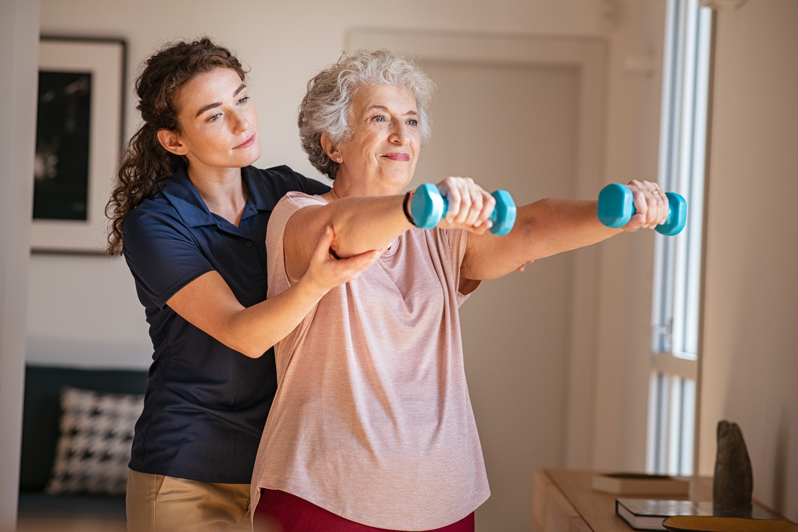 Physical therapy professional helping an elderly woman lift weights