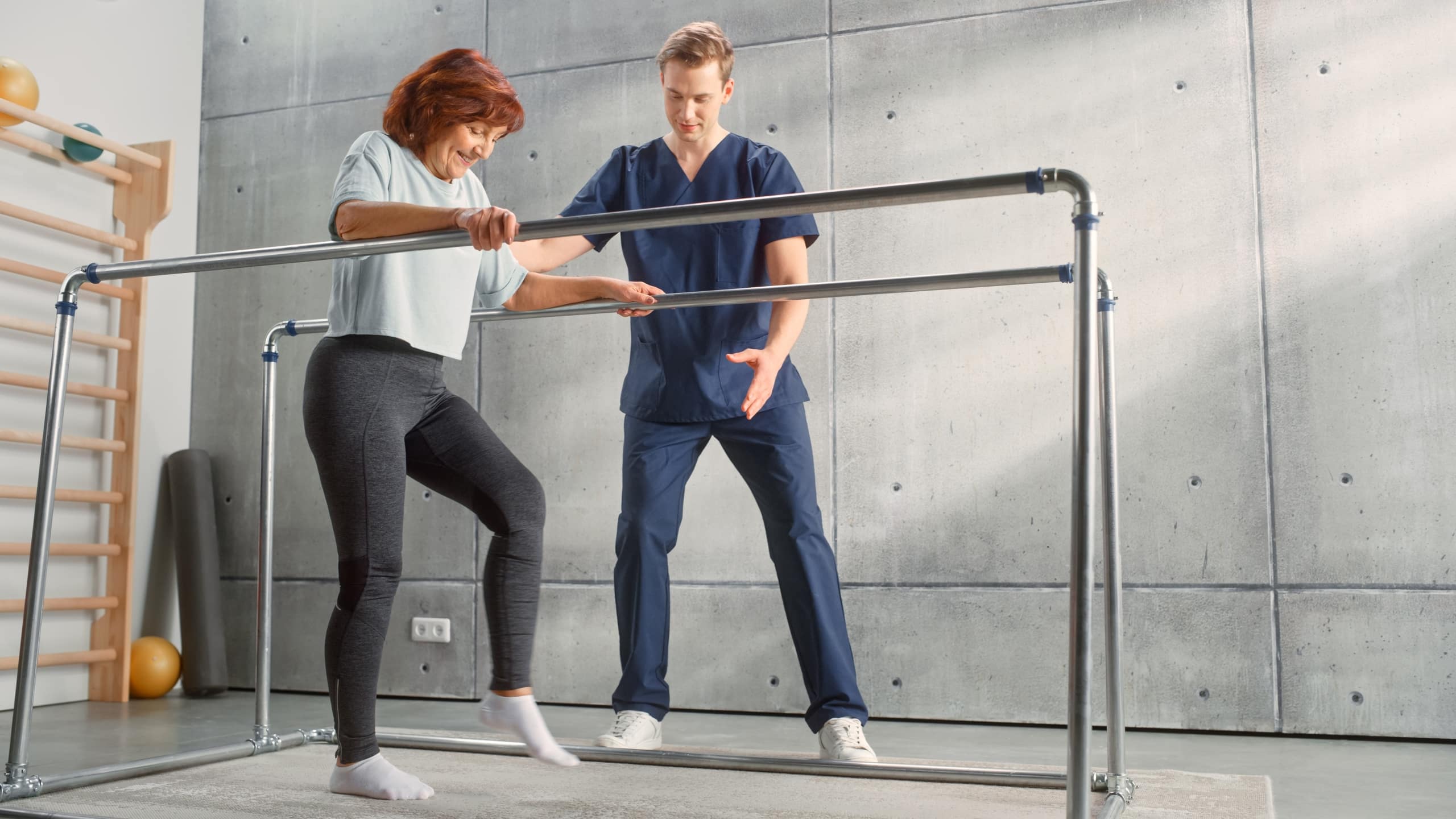 Physical therapy professional helping a patient use parallel bars