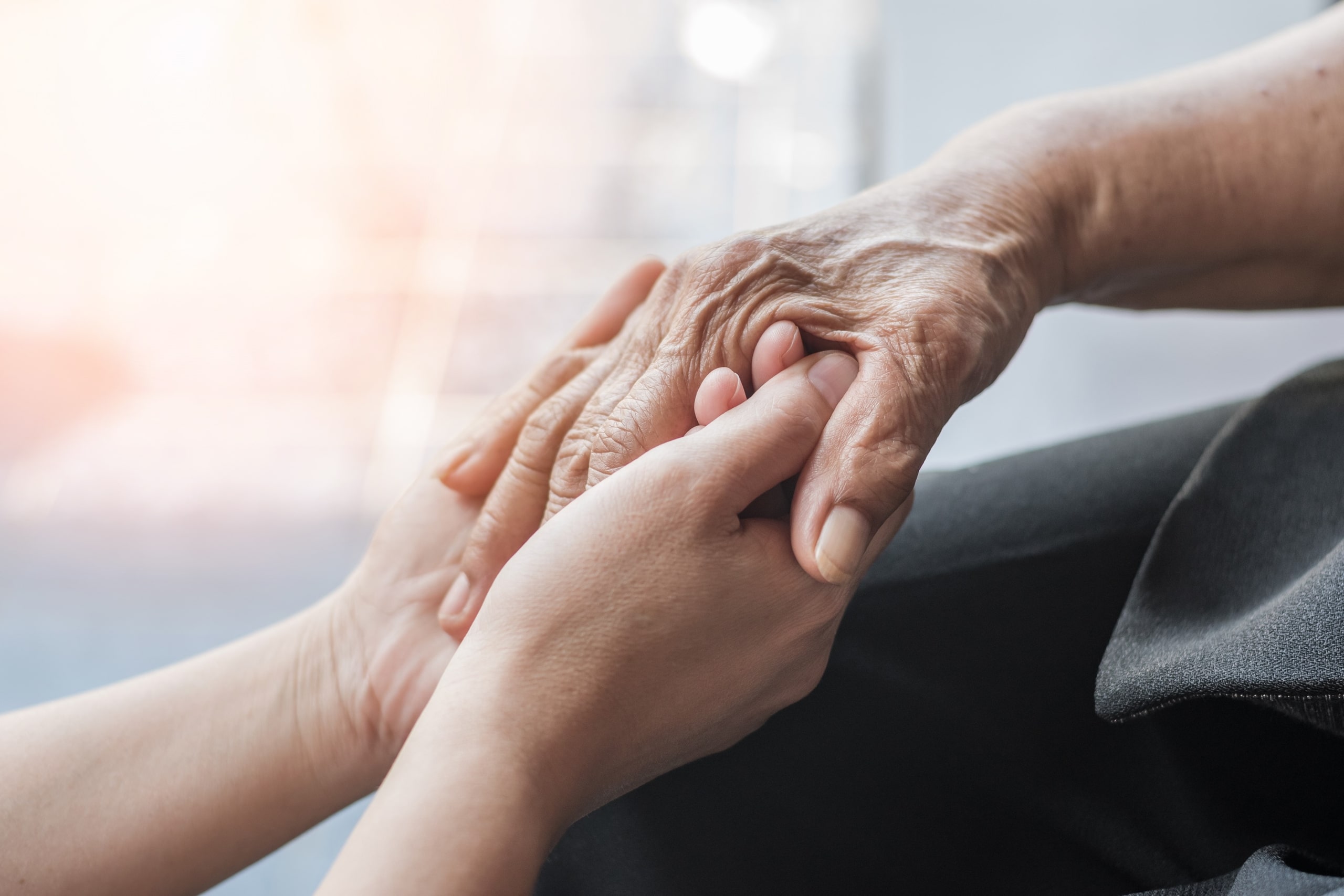 Close up of a healthcare professional holding the hand of an elderly person