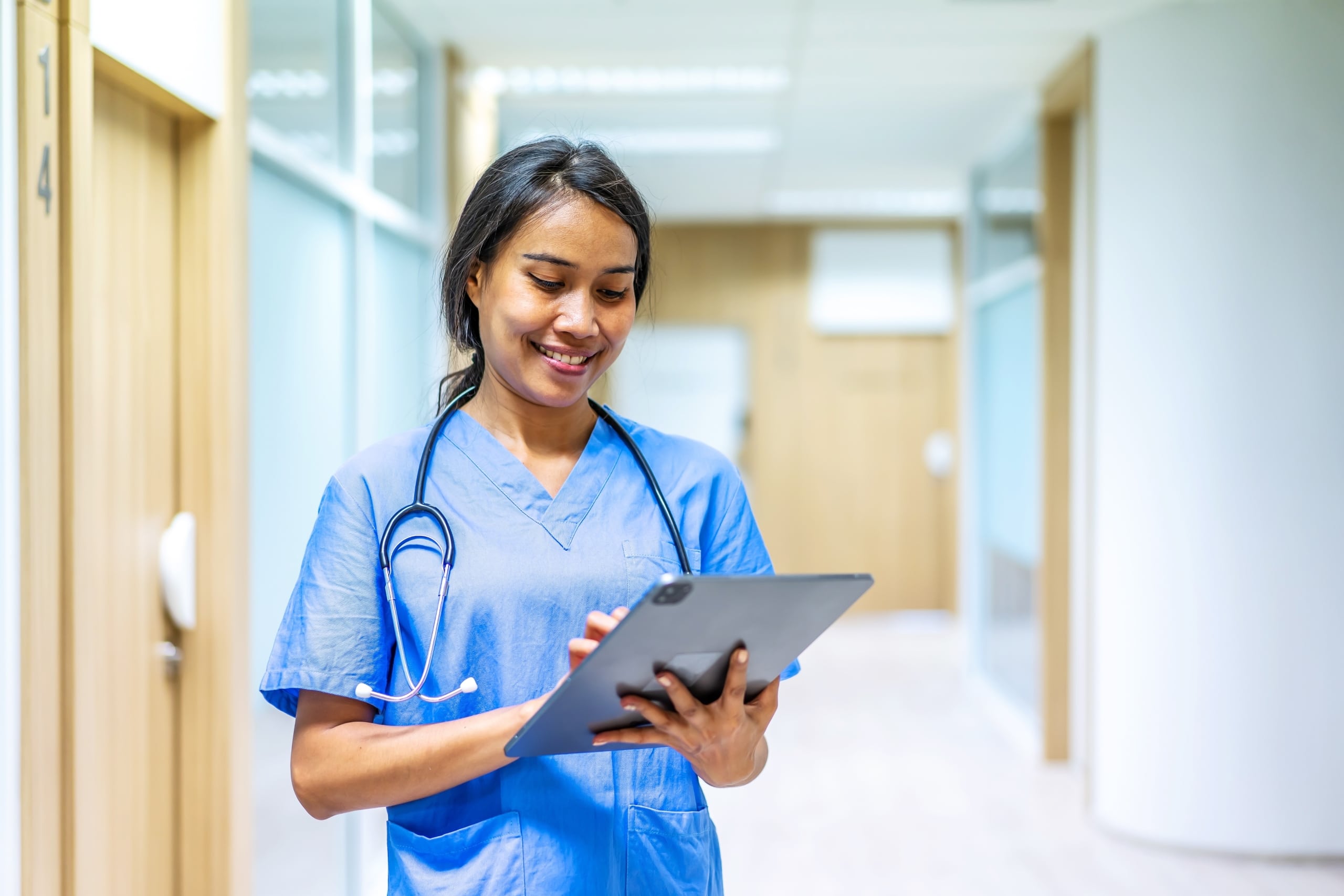Asian nurse in scrubs using a tablet in a hospital