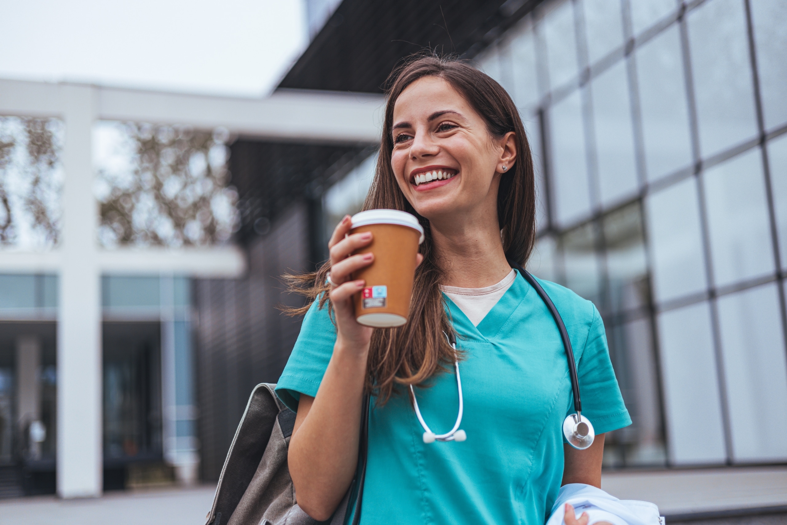 Nurse in scrubs holding a cup of coffee outside