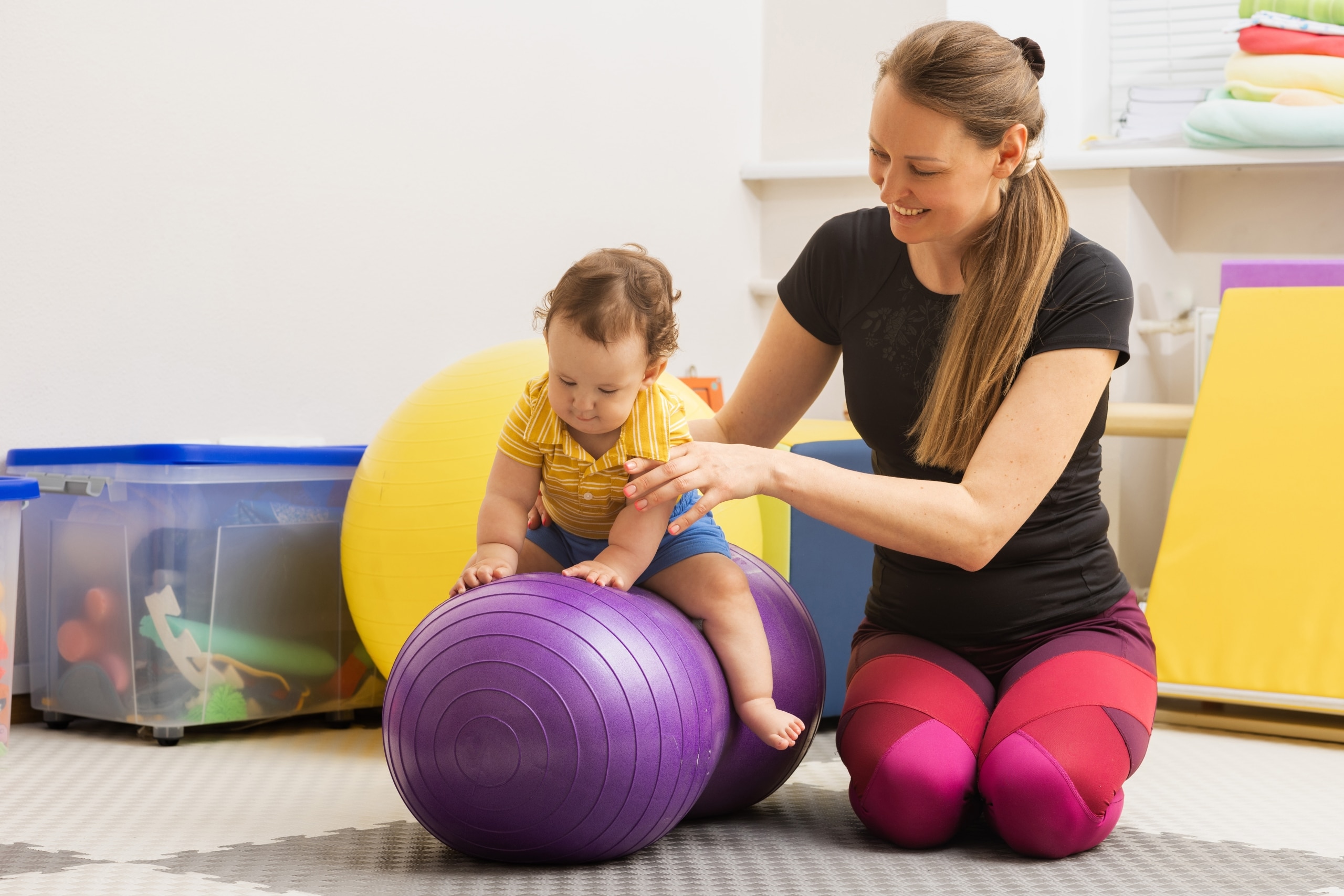 Occupational therapy professional helping a child balance on an exercise ball