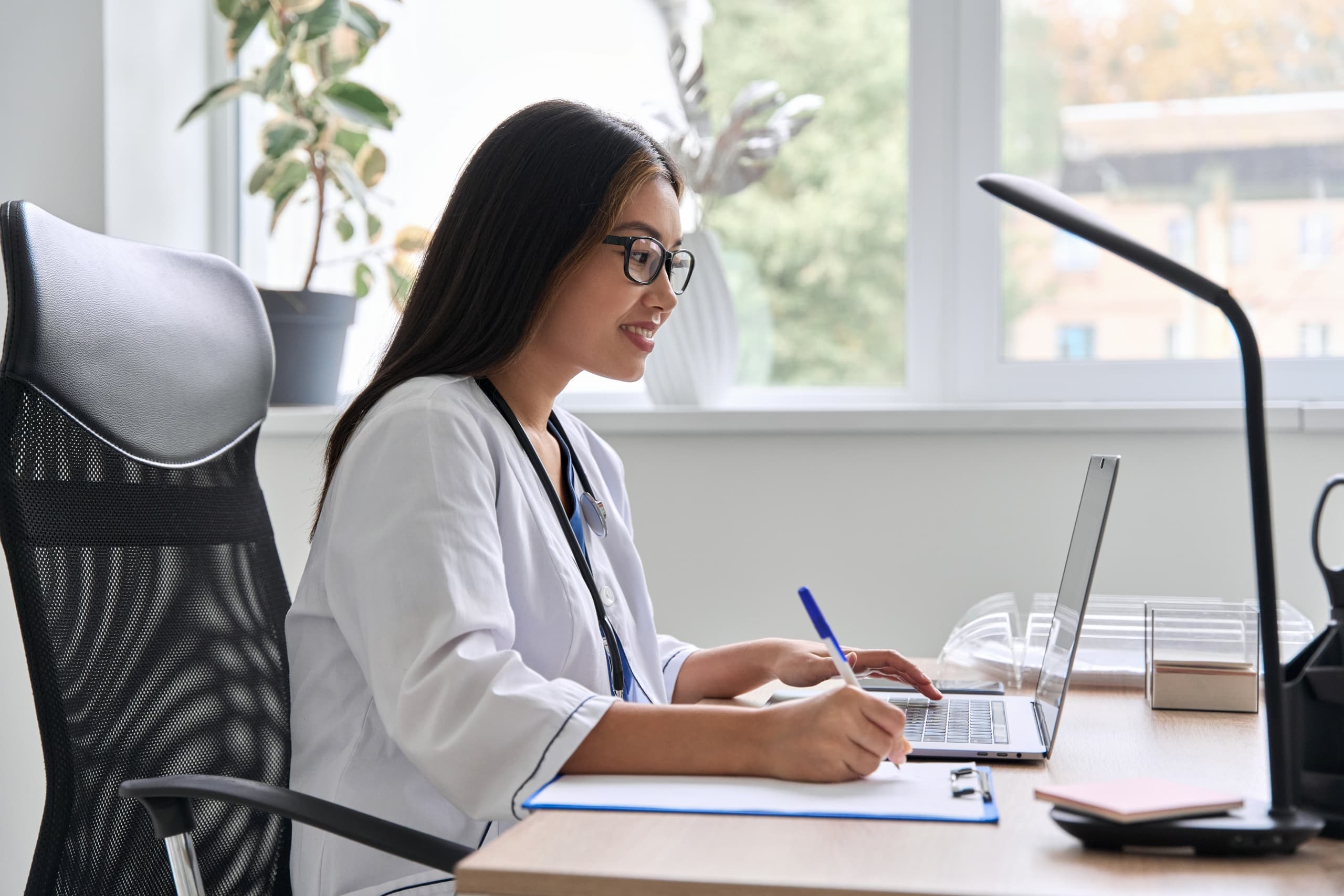 Asian medical professional taking notes and using a laptop