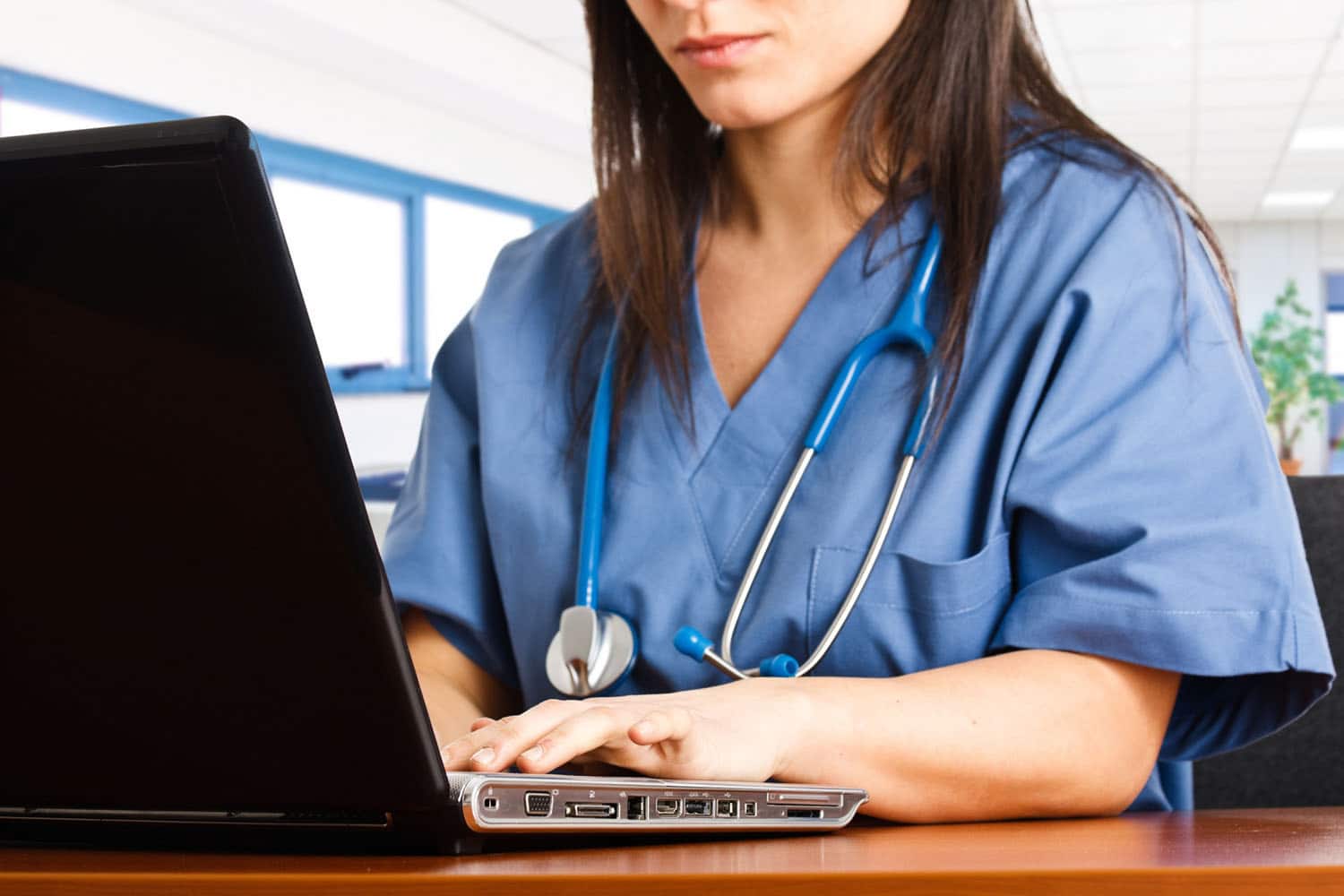 Close up of a nurse in scrubs typing on a laptop